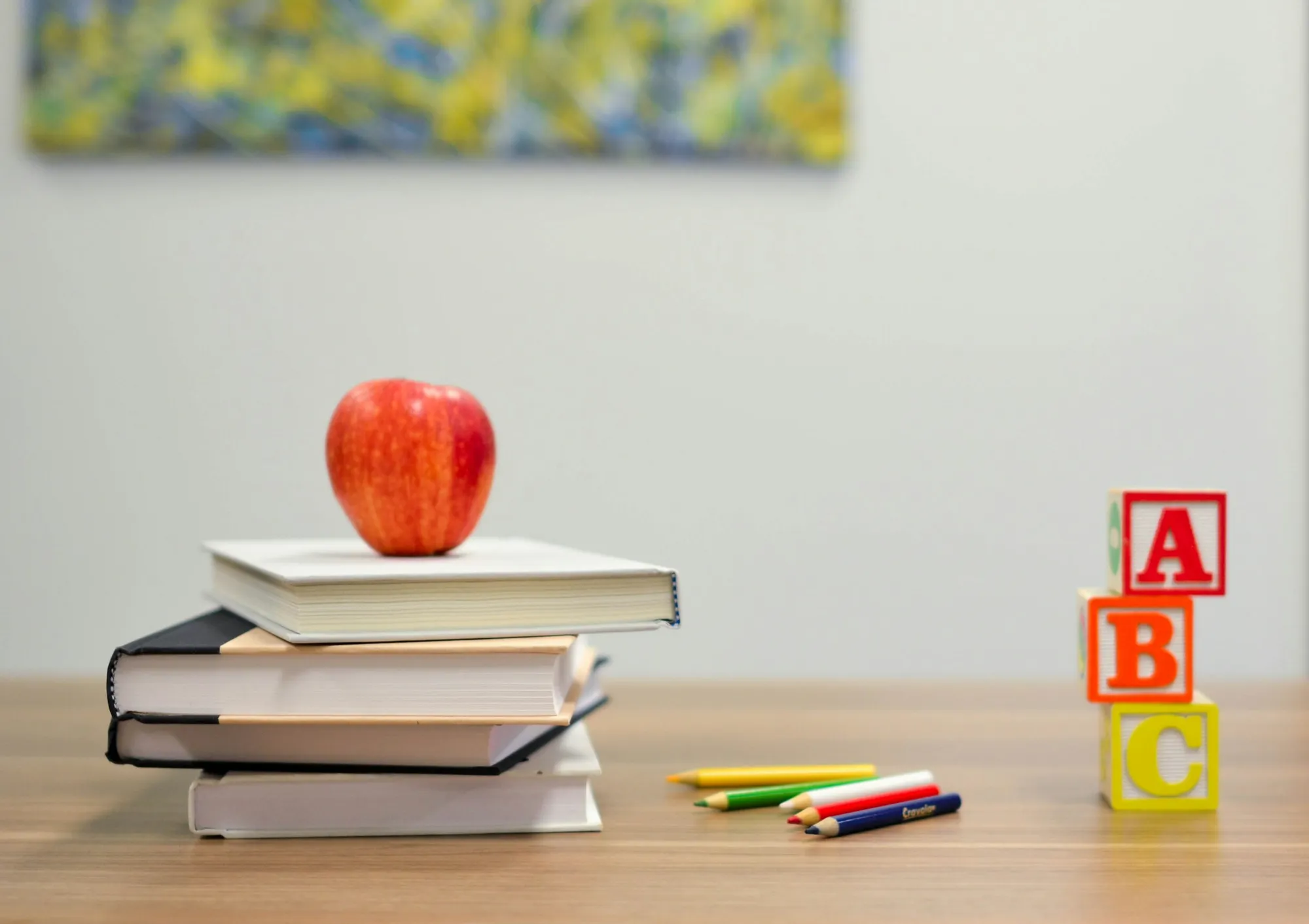 An apple on a classroom desk beside wooden alphabet blocks